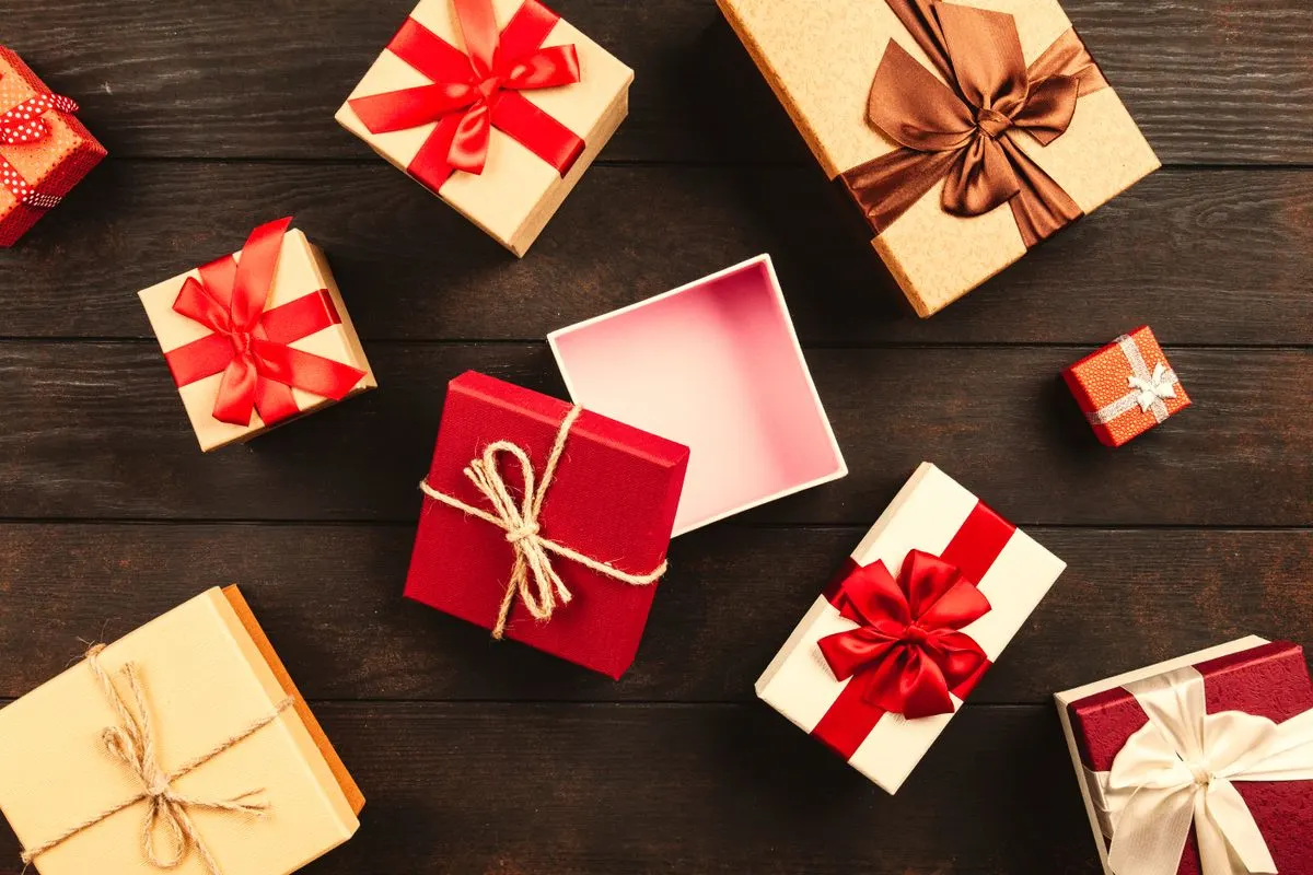 Nhiều hộp quà đỏ, trắng, vàng thắt nơ ruy băng trên mặt bàn gỗ